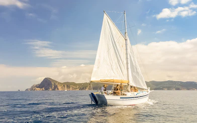 Tourists on a classic sailboat during a private sunset cruise near Ibiza's coastline.