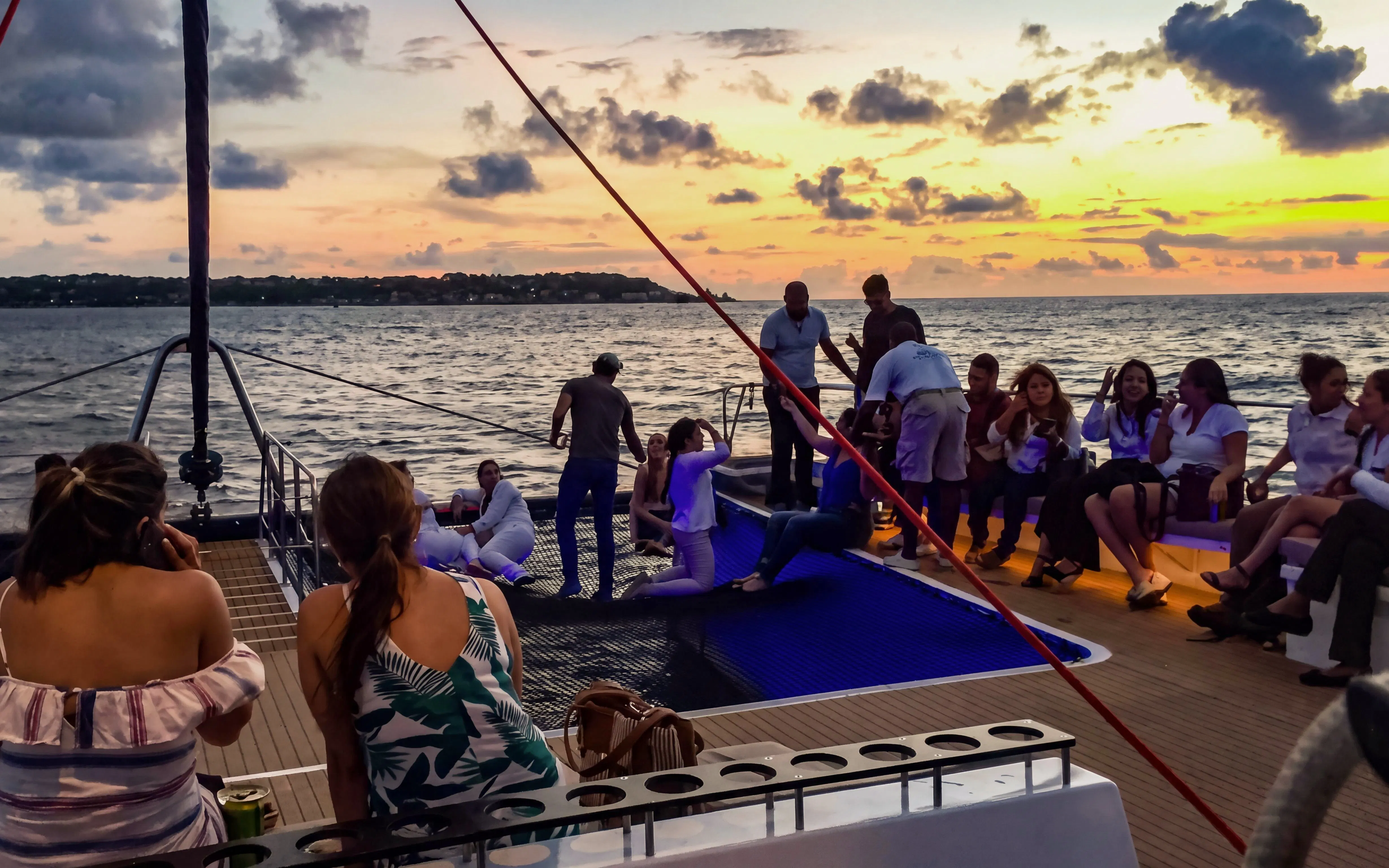 Sunset catamaran cruise with people relaxing on deck, Cartagena coastline in view.