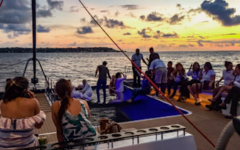 Sunset catamaran cruise with people relaxing on deck, Cartagena coastline in view.