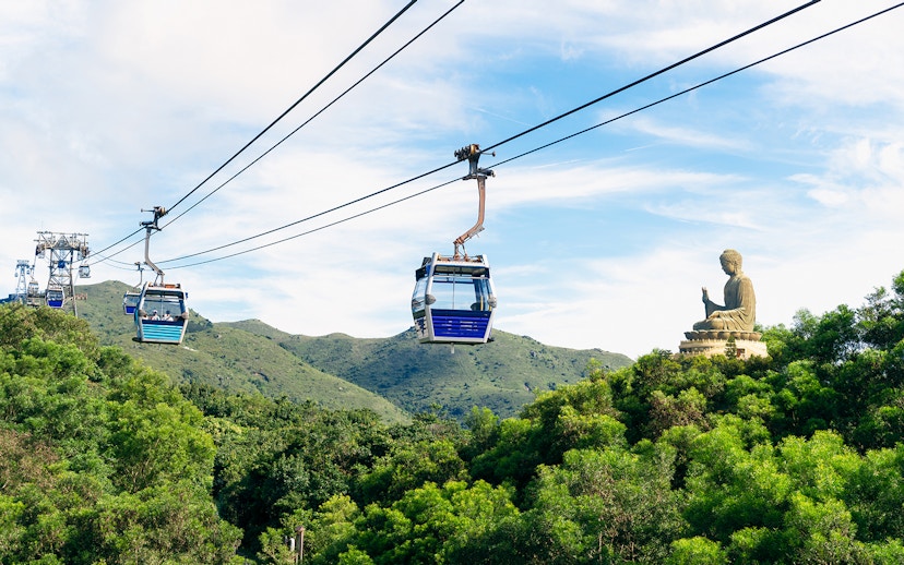 Cable cars over lush hills with Tian Tan Buddha in Ngong Ping, Hong Kong.