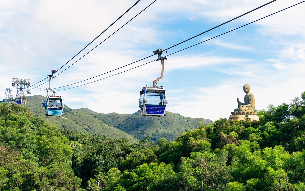 Cable cars over lush hills with Tian Tan Buddha in Ngong Ping, Hong Kong.