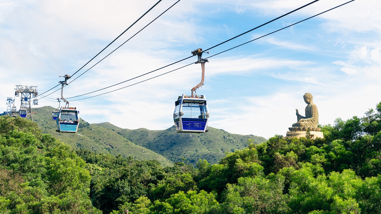 Cable cars over lush hills with Tian Tan Buddha in Ngong Ping, Hong Kong.