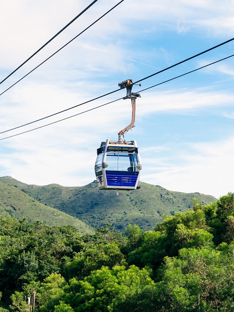 Cable cars over lush hills with Tian Tan Buddha in Ngong Ping, Hong Kong.