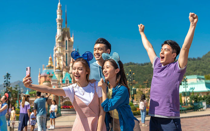 Visitors enjoying Hong Kong Disneyland with castle in background.