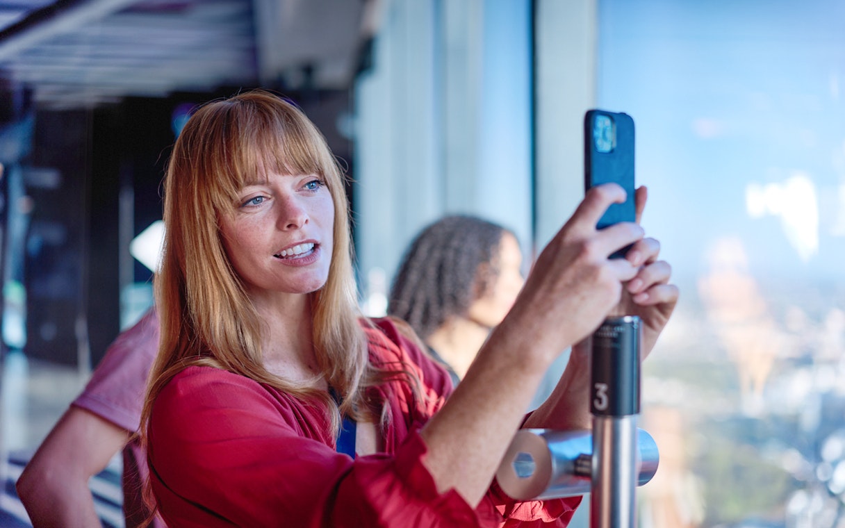 Person using a VR device at Melbourne Skydeck with city view in background.