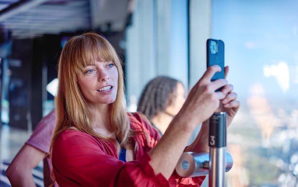 Person using a VR device at Melbourne Skydeck with city view in background.