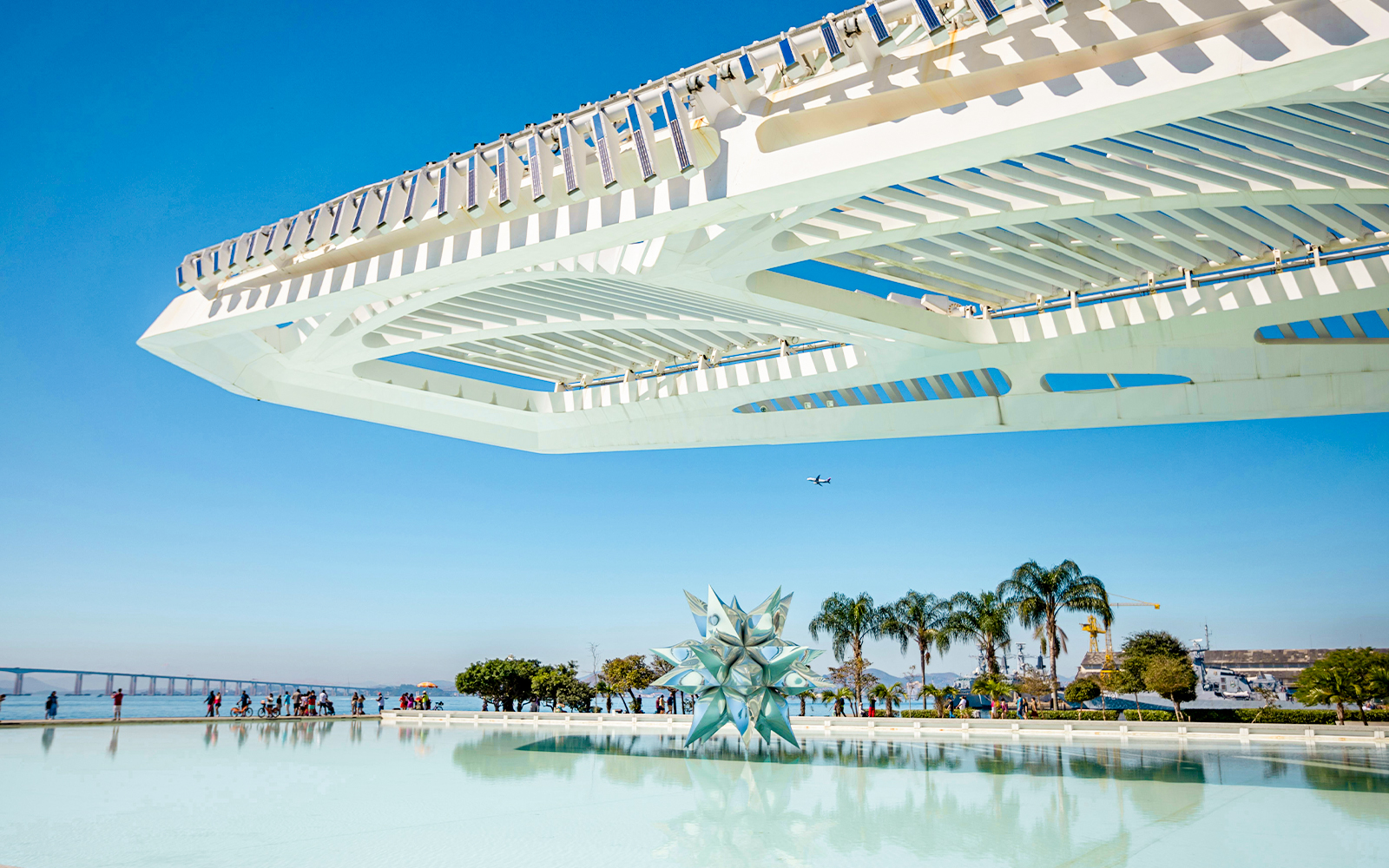 Futuristic architecture of Museu do Amanhã in Rio with water feature and palm trees.