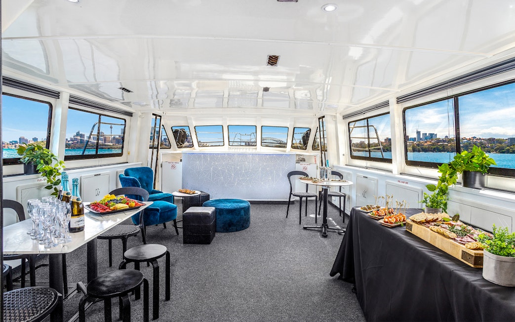 Interior of a Sydney cruise with canapés and drinks, featuring city views through large windows.
