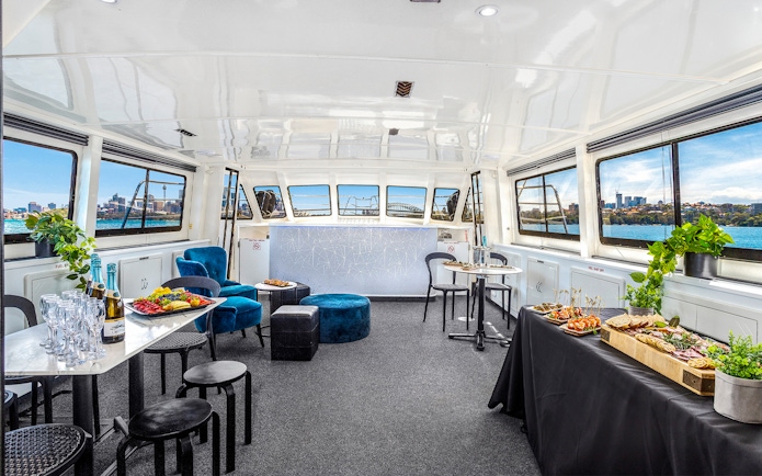 Interior of a Sydney cruise with canapés and drinks, featuring city views through large windows.