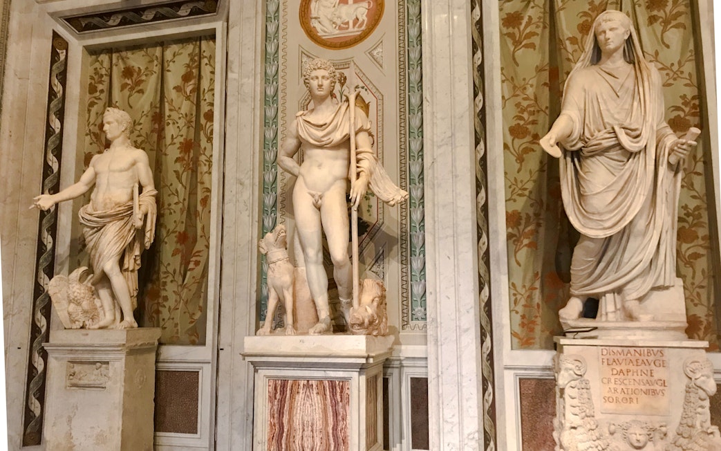 Marble statues in Borghese Gallery, Rome, depicting classical figures with intricate backgrounds.