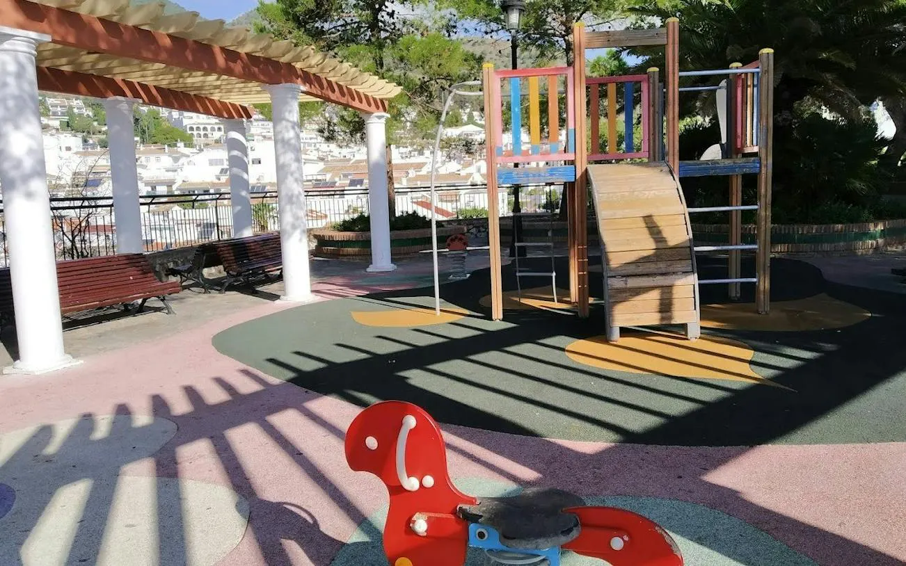 Playground in Benalmádena Pueblo with colorful equipment and village view in background.