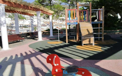 Playground in Benalmádena Pueblo with colorful equipment and village view in background.