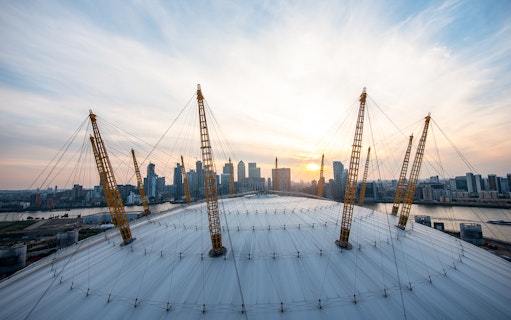 Climbers on the O2 Arena roof in London with city skyline at sunset.