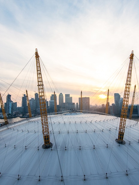 Climbers on the O2 Arena roof in London with city skyline at sunset.