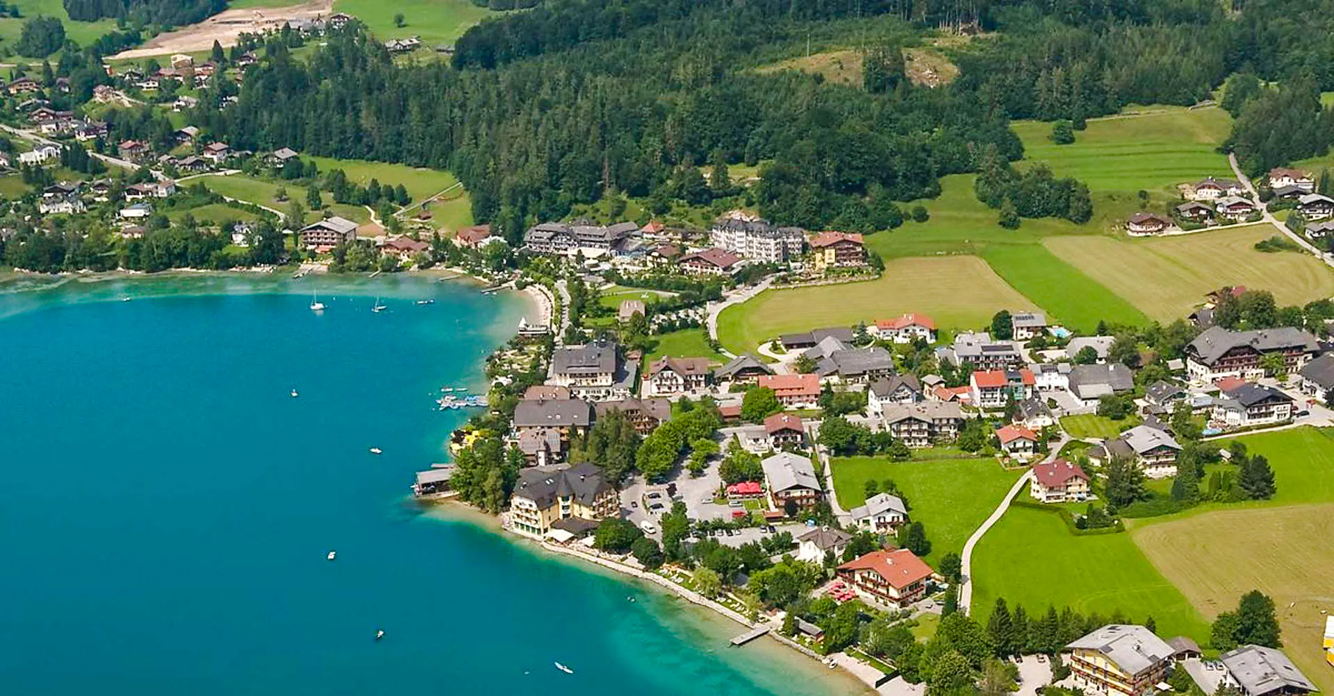 Aerial view of Hallstatt village by the lake with surrounding green fields and forests, Salzburg.