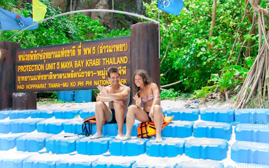 Couple sitting by Maya Bay sign, Phi Phi National Park, Thailand.