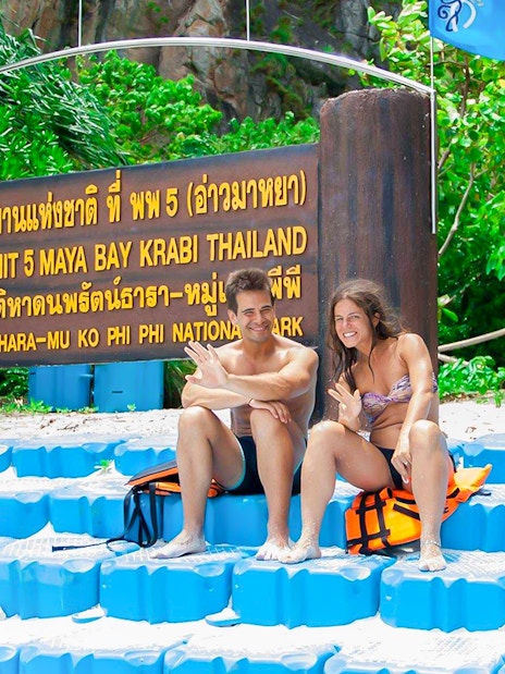 Couple sitting by Maya Bay sign, Phi Phi National Park, Thailand.