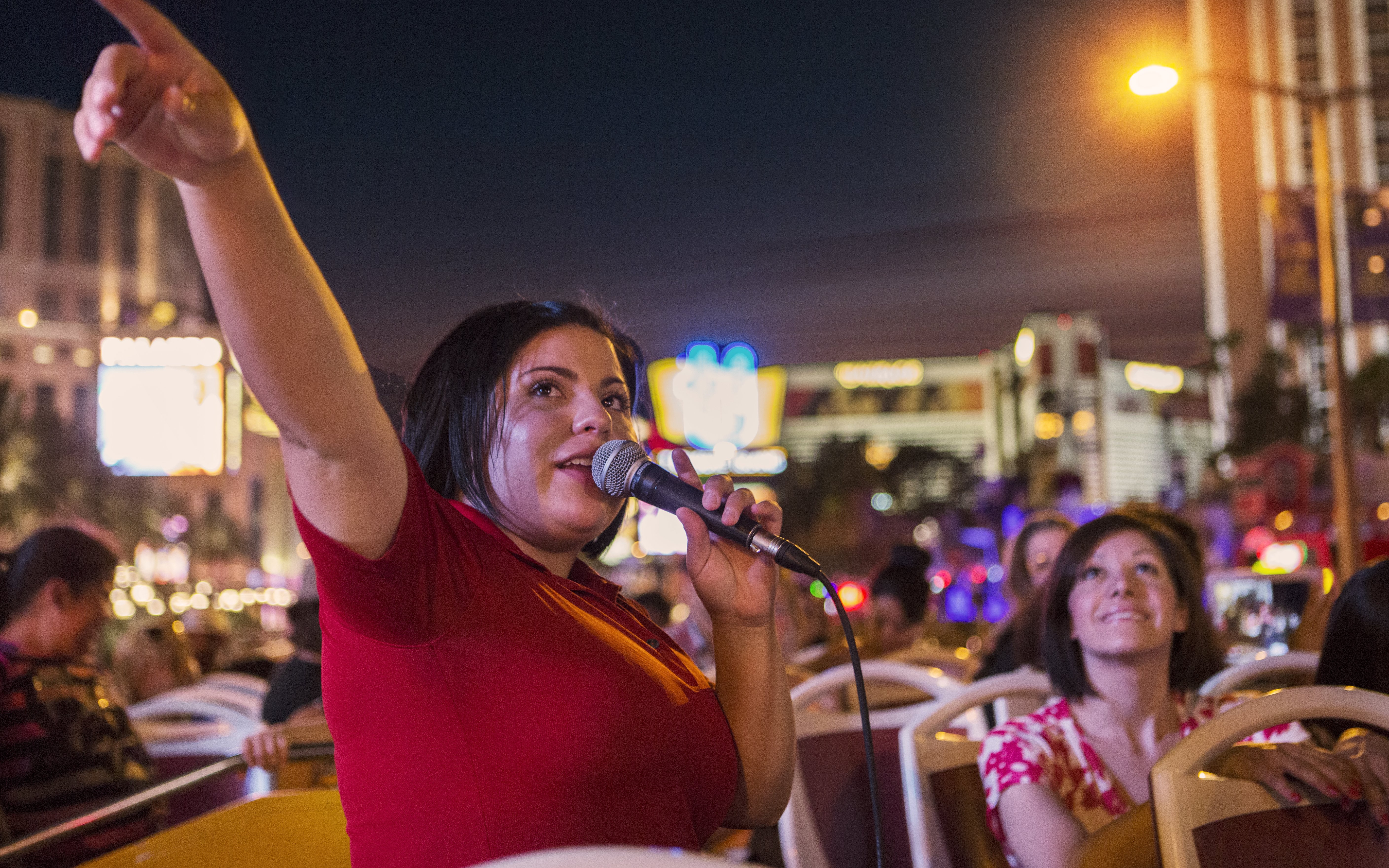 Tour guide speaking on a Dublin night bus tour with city lights in the background.