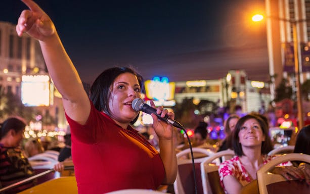 Tour guide speaking on a Dublin night bus tour with city lights in the background.