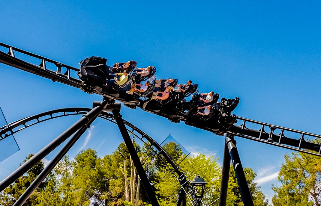 Parque Warner Madrid roller coaster with Warner Bros characters and visitors enjoying the ride.