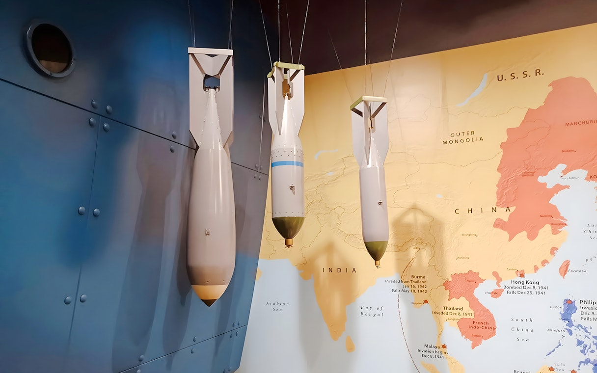 World War II bombs displayed against a map backdrop at USS Arizona tour exhibit.