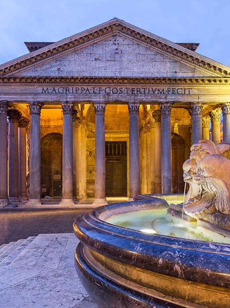 Pantheon in Rome with illuminated fountain at sunset.