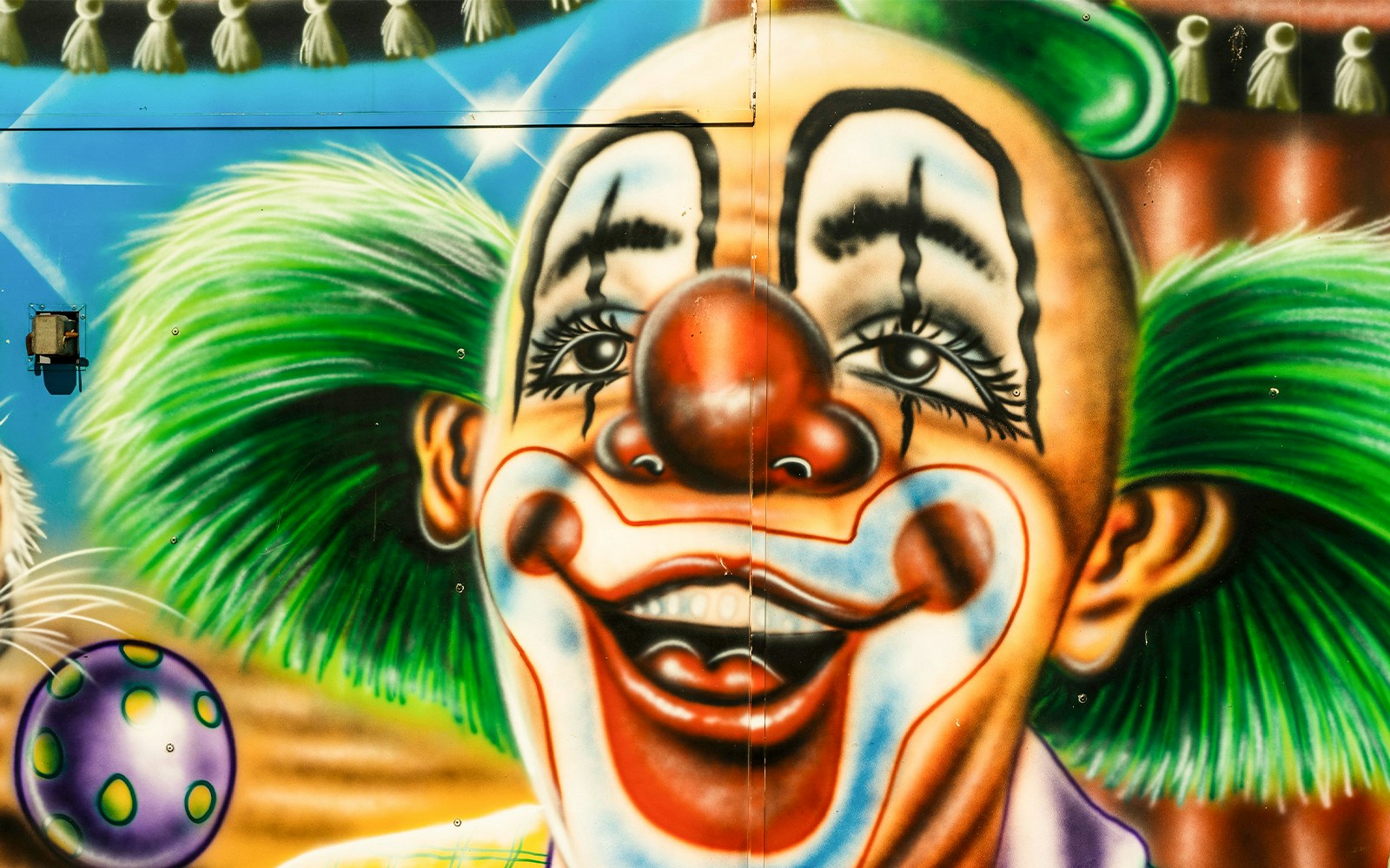 Clown face mural with green hair and red nose on a colorful surface.