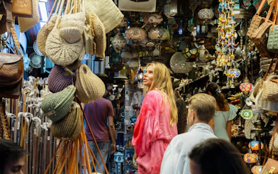 Tourists exploring Muttrah Souk with hanging lanterns and woven bags in Muscat, Oman.