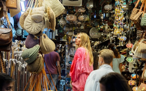 Tourists exploring Muttrah Souk with hanging lanterns and woven bags in Muscat, Oman.