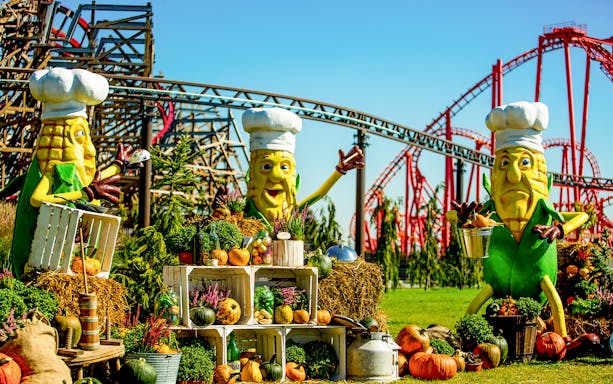 Energylandia Halloween display with corn mascots and pumpkins near roller coasters.