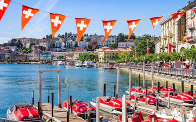 Lake Lugano waterfront with red pedal boats and Swiss flags, Switzerland.