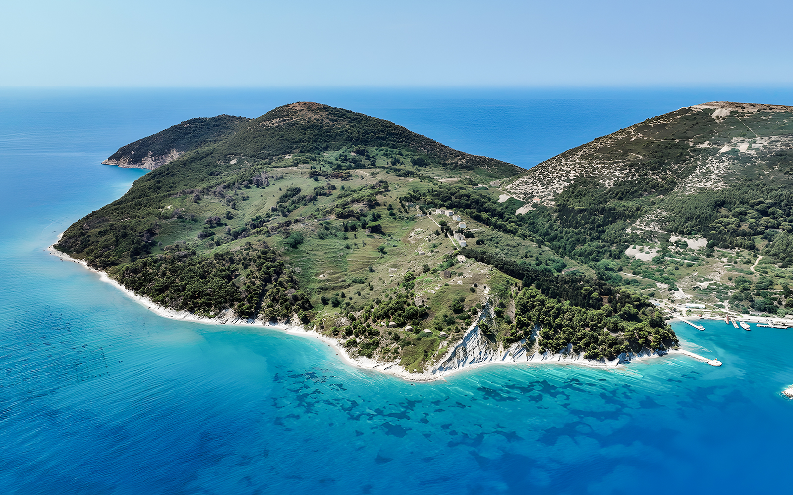 Aerial view of lush green peninsula with turquoise waters, part of Vlora's Ionian Odyssey, Albania.