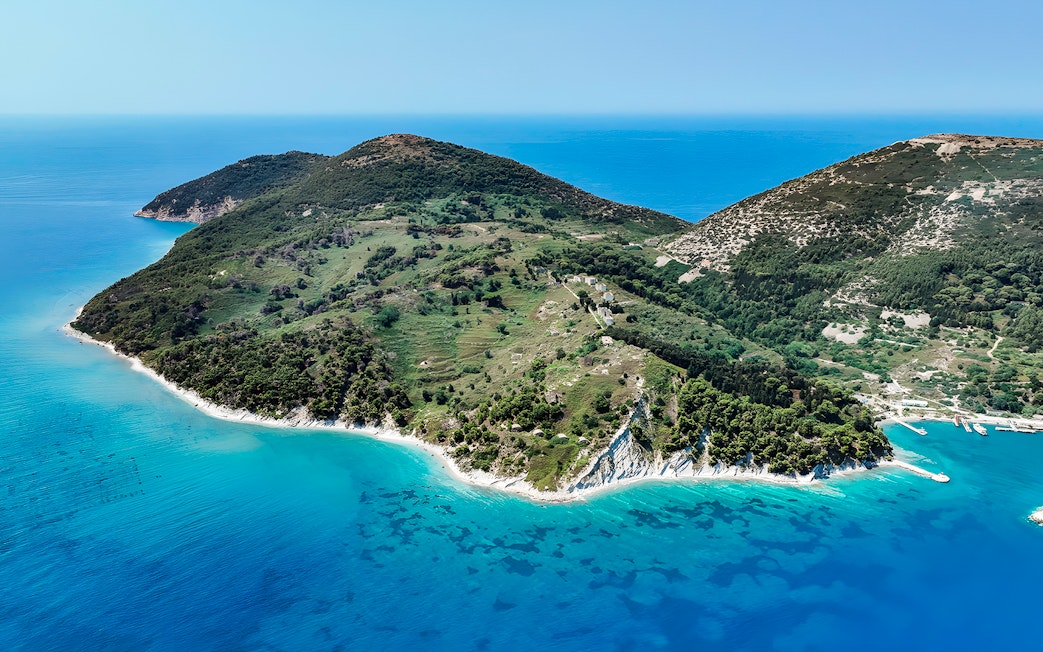 Aerial view of lush green peninsula with turquoise waters, part of Vlora's Ionian Odyssey, Albania.