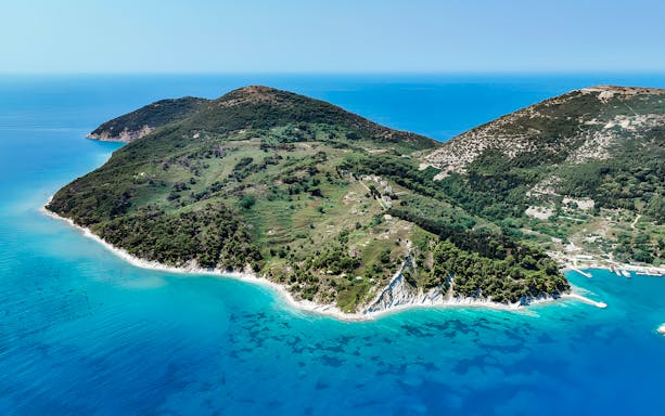 Aerial view of lush green peninsula with turquoise waters, part of Vlora's Ionian Odyssey, Albania.