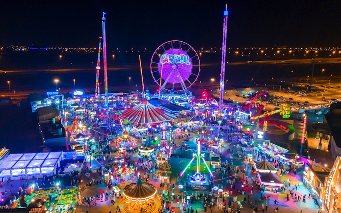 Aerial view of Global Village Dubai at night with colorful lights and Ferris wheel.