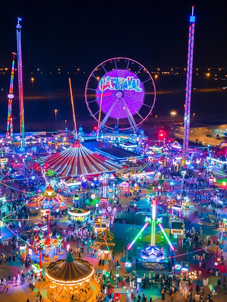 Aerial view of Global Village Dubai at night with colorful lights and Ferris wheel.