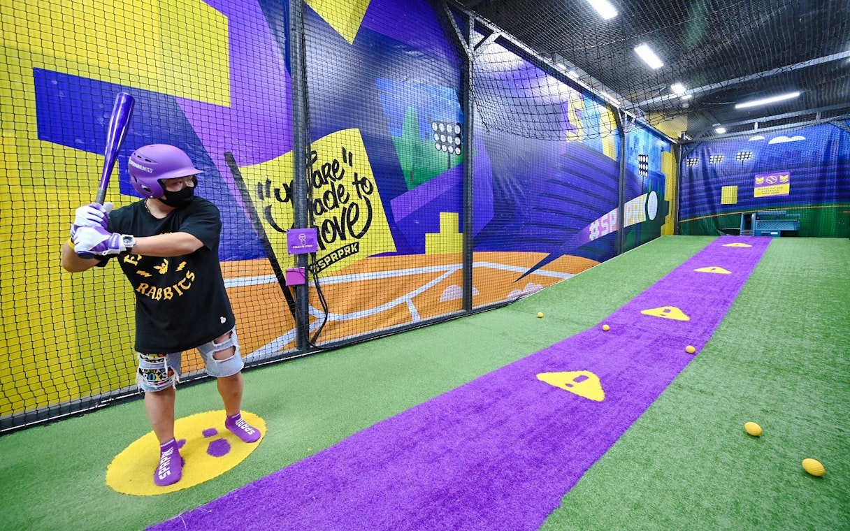 Man practicing baseball in a netted area at SuperPark Singapore.