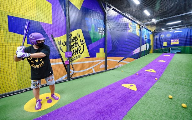 Man practicing baseball in a netted area at SuperPark Singapore.
