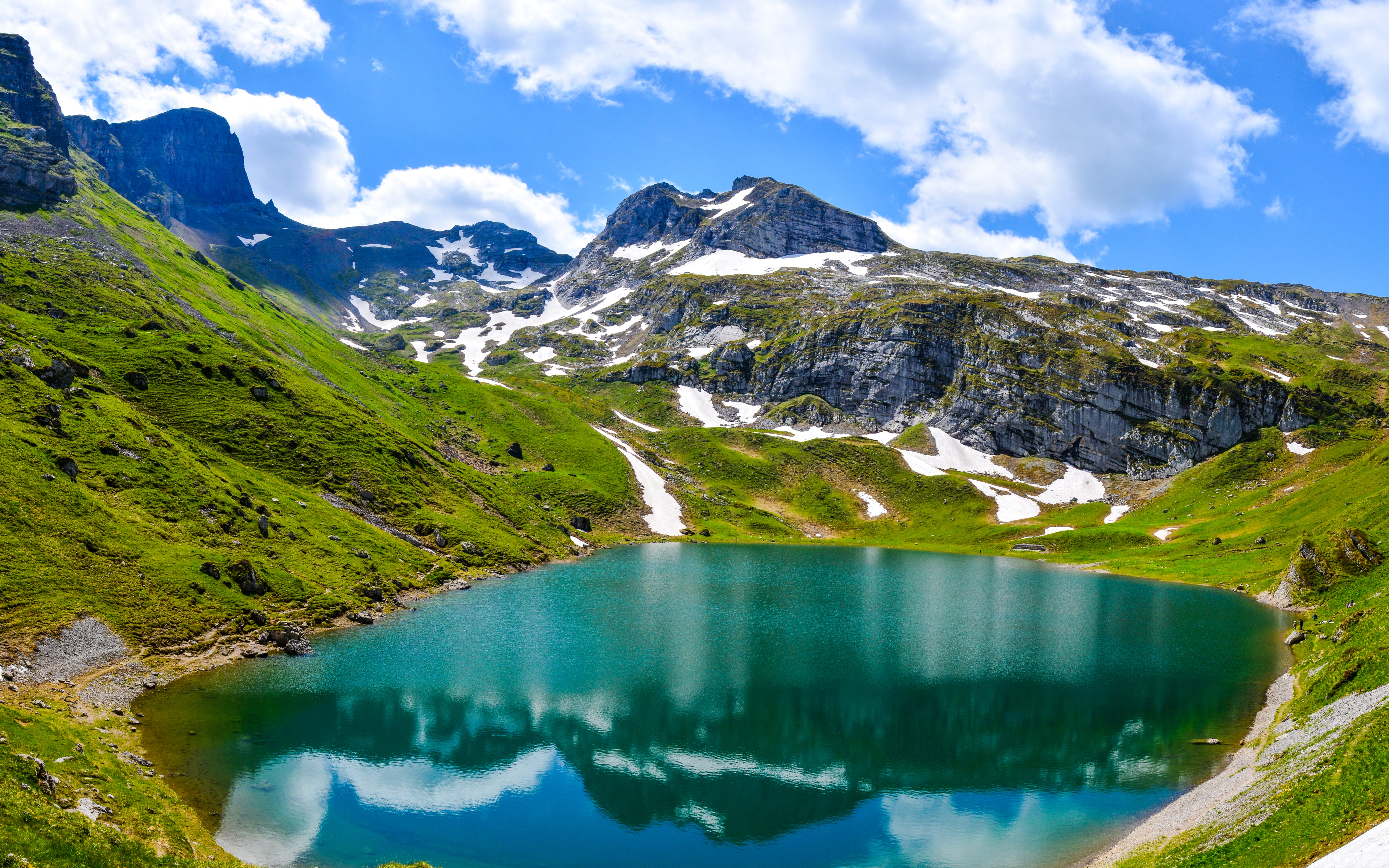 Alpsee Lake Park with clear blue water and surrounding snow-capped mountains.