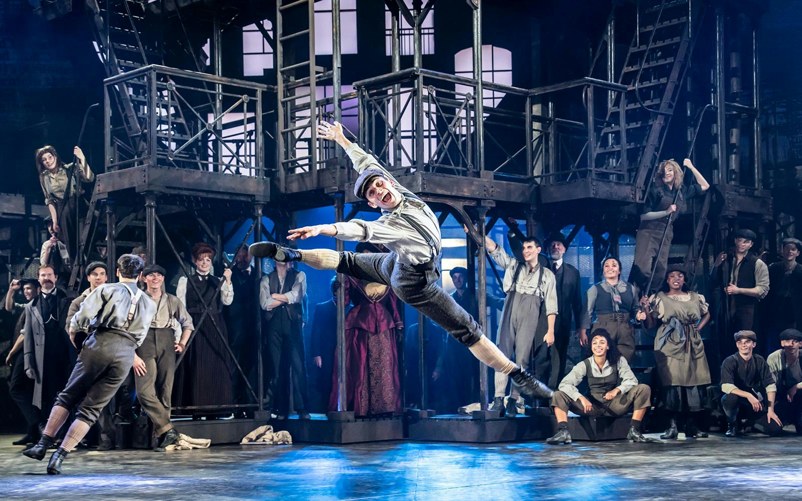 Performer leaping on stage during a Newsies musical production.