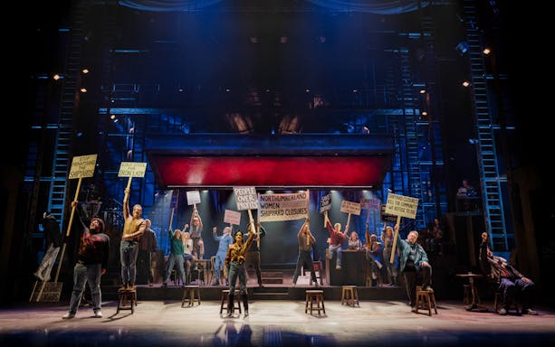 Stage performance of "The Last Ship" in Brisbane with actors holding protest signs.