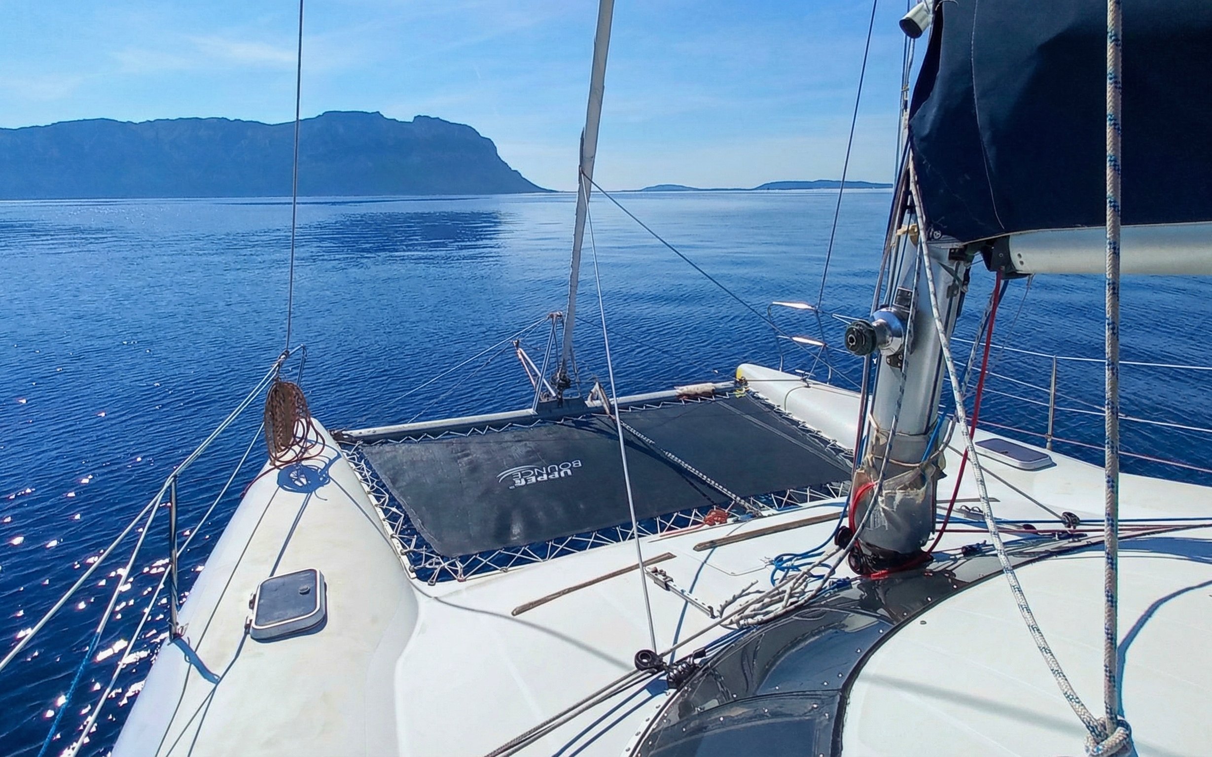 Catamaran sailing near Tavolara Island with clear blue waters and distant land view.
