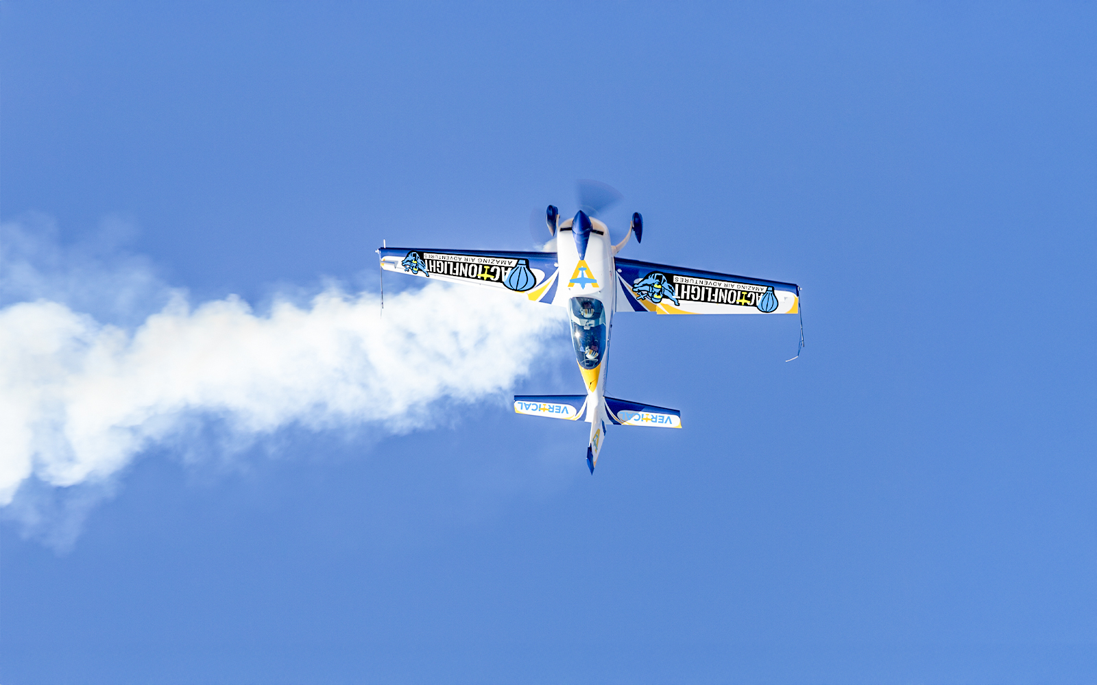 Aerobatic plane performing a stunt with smoke trail against clear blue sky.