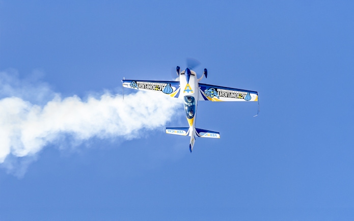 Aerobatic plane performing a stunt with smoke trail against clear blue sky.