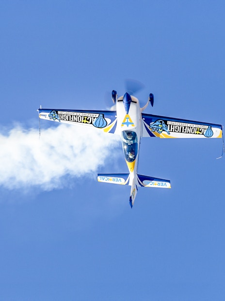 Aerobatic plane performing a stunt with smoke trail against clear blue sky.
