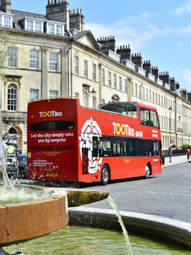 Red Tootbus in Bath passing historic Georgian buildings.