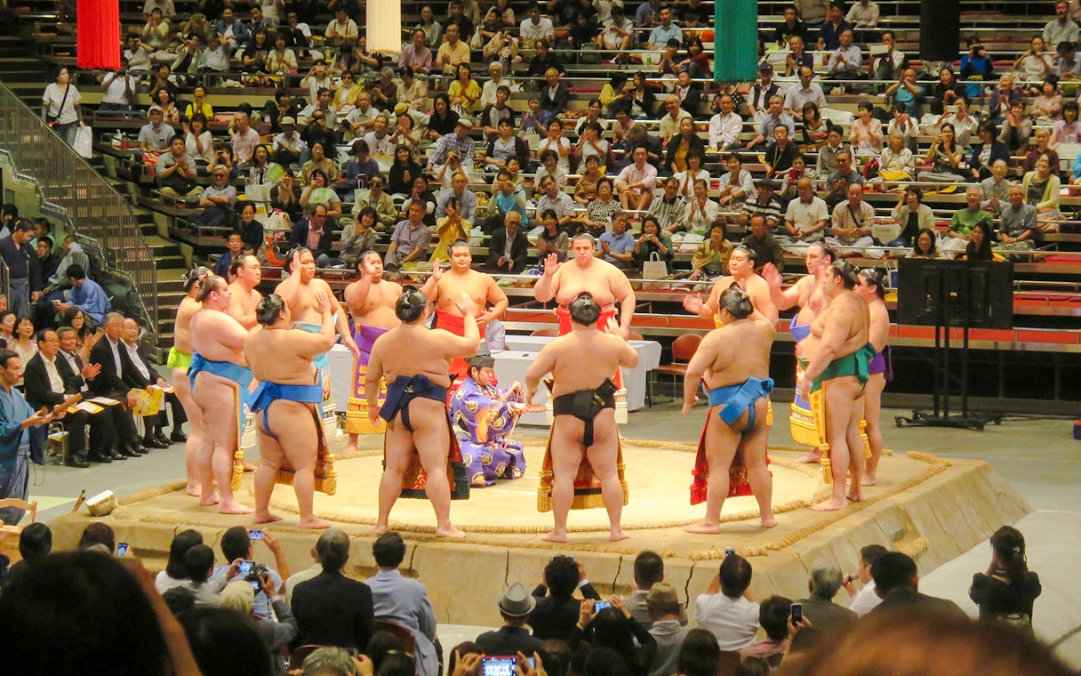 Sumo wrestlers in a ring with a large crowd watching in Tokyo.