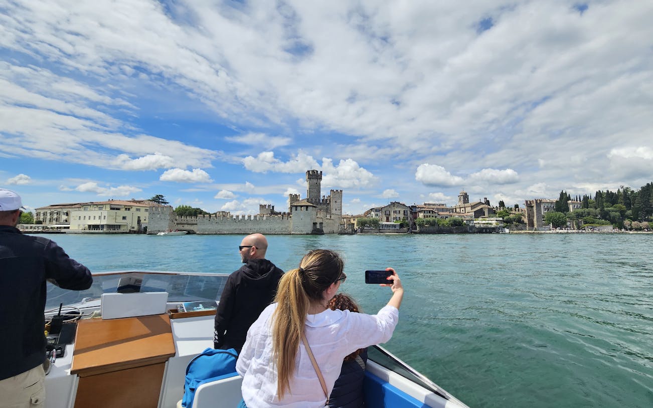 Private boat tour with people viewing Sirmione Castle on Lake Garda, Italy.