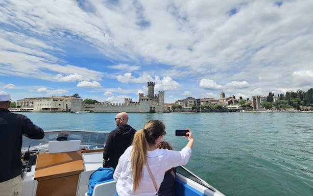 Private boat tour with people viewing Sirmione Castle on Lake Garda, Italy.