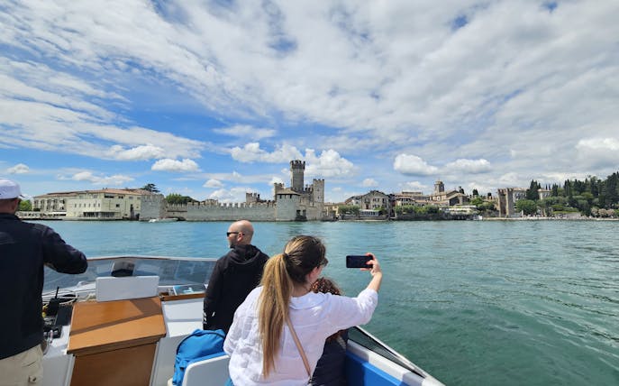 Private boat tour with people viewing Sirmione Castle on Lake Garda, Italy.